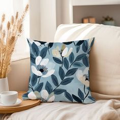 a blue flowered pillow sitting on top of a white couch next to a cup