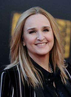 a woman with long blonde hair smiling at the camera and wearing a black suit jacket