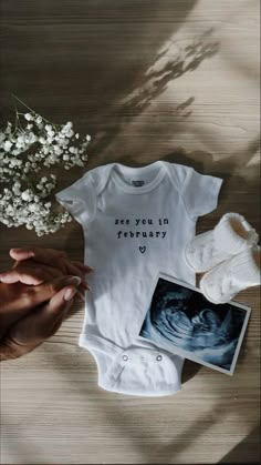 someone is holding their baby's hand next to the birth announcement shirt and booties