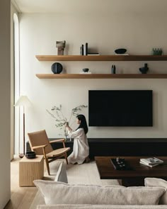 a woman is sitting on the floor in her living room and looking at the television