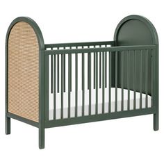 a green crib with a wicker bed and white sheets on the bottom half