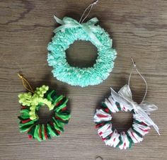 three christmas wreaths hanging from strings on a wooden table next to scissors and yarn