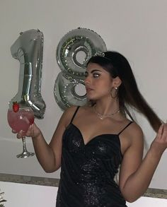 a woman in a black dress holding up a balloon and a glass with the number eighty