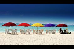 people sitting under umbrellas on the beach with chairs and tables in front of them