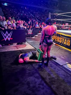 the wrestler is laying on the ground as his opponent stands next to him in front of an audience