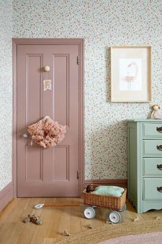 a pink door in the corner of a room next to a green dresser and chest