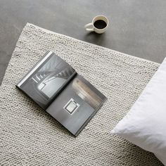 an open magazine sitting on top of a rug next to a pillow and cup of coffee