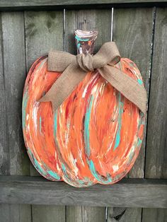 a painted pumpkin sitting on top of a wooden fence next to a jar with a bow