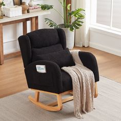 a black rocking chair with a blanket on top of it and a potted plant in the background