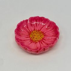 a pink flower sitting on top of a white table next to a red bowl with yellow center