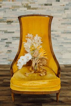 a yellow chair with flowers in it on a wooden floor next to a brick wall