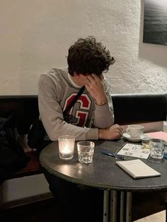 a man sitting at a table with his head in his hands and writing on a piece of paper