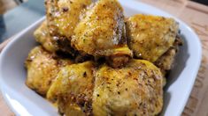 a white bowl filled with chicken wings covered in gravy and seasoning on top of a wooden table