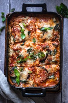 a casserole dish with spinach, cheese and sauce in it on a wooden table