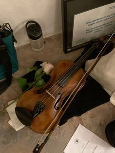 a violin is laying on the ground next to a bag and some papers with flowers