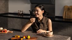 a woman sitting at a kitchen table with food on the counter and in front of her