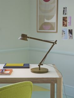 a desk lamp sitting on top of a wooden table next to a green chair in a room