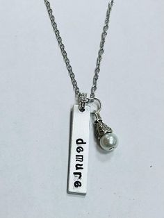 Demure Necklace - The bar charm is handstamped and is one and a quarter inch in length and one quarter inch wide, made of non tarnish aluminum. I stamp Demure on the charm. It comes on an approximately 18 inch stainless steel chain (does not tarnish) with a secure lobster claw clasp. It clusters together with a small glass white pearl dangle. Inspired by the viral quote "very cutesy, very sweet, very demure." A great gift! Because this item is handstamped, expect some slight variation in the lettering, but that is to be expected and is what makes it charming. Handmade in America. Very Demure, Necklace Quotes, Fashion Jewelry Necklaces, Bar Necklace, Steel Chain, White Pearl, Stainless Steel Chain, Link Chain, Lobster Claw