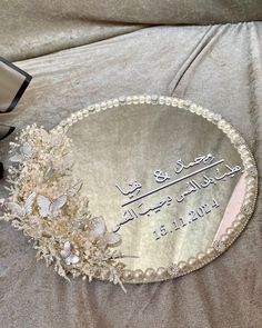 a personalized glass plaque with flowers and pearls sits on a bed next to an open book