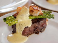 a piece of steak with asparagus, scallops and sauce on it