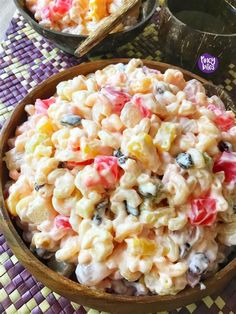 a bowl filled with macaroni salad on top of a purple place mat next to two bowls