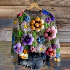 a sweater with colorful flowers on it hanging from a wooden hanger next to a wood wall