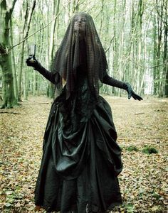 a woman dressed in black standing in the woods