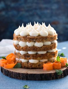 a layered cake with white frosting and carrots on a wooden board next to a blue table cloth