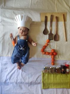 a baby wearing a chef's hat and overalls next to various kitchen utensils