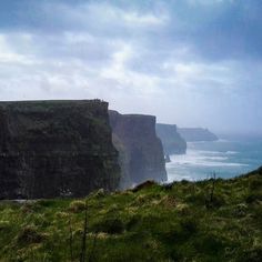 sheep standing on the edge of a cliff overlooking the ocean with cliffs in the background