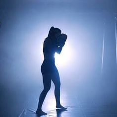 a woman standing in front of a spotlight on a stage with her hands behind her head