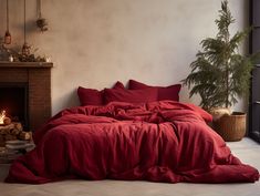 a bed with red sheets and pillows next to a fireplace