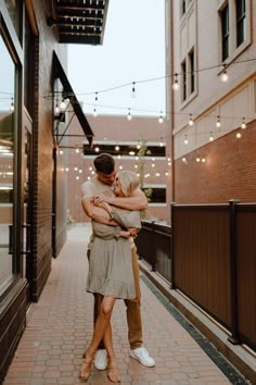 a man and woman embracing each other in an alleyway with string lights strung overhead