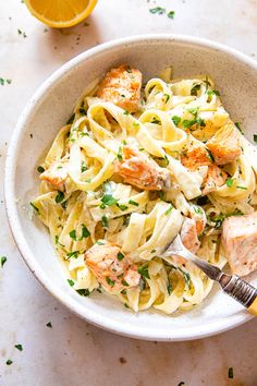 a white bowl filled with pasta and salmon on top of a table next to an orange slice