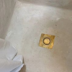 a gold vent in the corner of a white room with sheets on the floor and an open toilet paper dispenser next to it