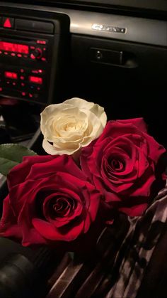 three roses sitting on top of a table in front of a car stereo and dash board