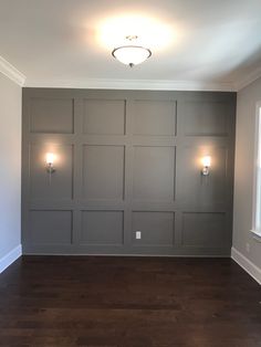 an empty room with wood flooring and gray paneling on the walls, along with two lights