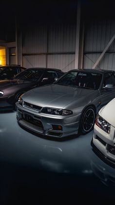 several cars are parked in a garage at night, one is silver and the other is white