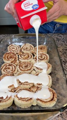 cinnamon rolls being poured onto a baking sheet with icing on it and someone pouring milk over the top