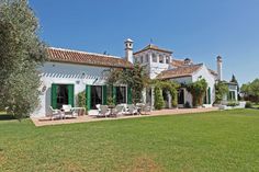 a large white house with green shutters and an olive tree in the front yard