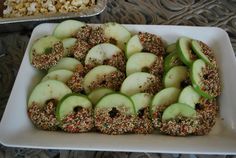 apples and nuts are arranged on a white platter next to a tray of popcorn