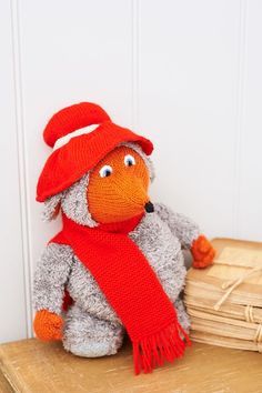 a stuffed animal wearing a red hat and scarf sitting on top of a wooden table