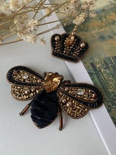 two bee brooches sitting on top of a white table next to some flowers