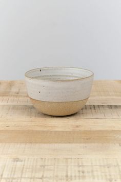 a white and brown bowl sitting on top of a wooden table next to a wall