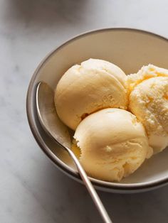 three scoops of ice cream sit in a bowl with a spoon on the side