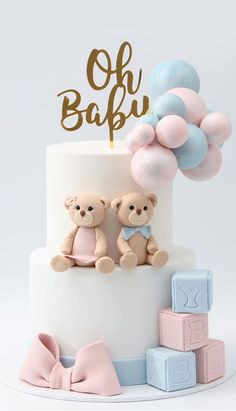 a white cake with two teddy bears on top and pink, blue and gold balloons