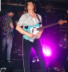 a man standing on top of a stage holding a blue and white guitar in his hand