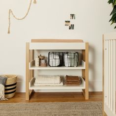 a white shelf with baskets and towels on it next to a plant in a room