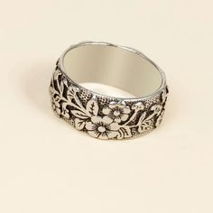 a silver ring with flowers and leaves on the inside, sitting on a white surface