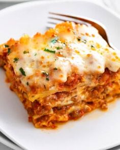 a white plate topped with lasagna covered in sauce and cheese next to a fork